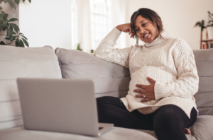 Pregnant woman sitting on couch in front of an open laptop and smiling.