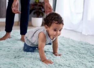 An infant crawls on a rug